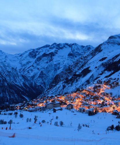Foto della stazione sciistica francese Les Deux Alpes di sera. Si può vedere una parte della località con molte montagne intorno.